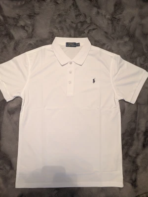 Vit pikétröja från Polo Ralph Lauren - Klassisk vit pikétröja från Polo Ralph Lauren med korta ärmar och krage. Storlek M/L.