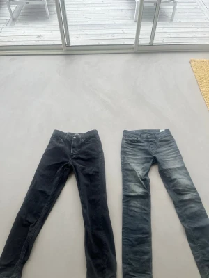 Två par smala jeans i svart och blått - Säljer två par jeans med smal passform, ett par i svart och ett par i tvättad blå denim. Båda har klassisk femficksdesign och normal midja. Perfekta för dig som gillar en enkel och stilren look. Materialet är bomullsdenim med stretch för extra komfort.