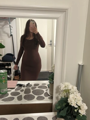 Brun långärmad långklänning - Snygg brun långklänning med lång ärm och rund halsringning. Klänningen har en figurnära passform och är tillverkad i ett stretchigt material som sitter bekvämt mot kroppen. Det är storlek Xs. Den är helt ny och aldrig använd 