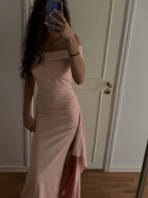 Ljusrosa axelbandslös långklänning - Trendig ljusrosa långklänning med offshoulder-design och hög slits på ena sidan. Klänningen har en åtsittande passform och är tillverkad i ett mjukt, stretchigt material som ger en elegant siluett. Perfekt för dig som vill sticka ut med en stilren look. Använd 2 gånger. Nypris 500kr