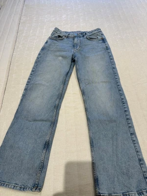 Blå raka jeans med vintagekänsla - Säljer ett par klassiska blå jeans med rak passform och lätt tvättad look. Jeansen har fem fickor, normal midja och är tillverkade i denim. Perfekta för en avslappnad och trendig stil. 