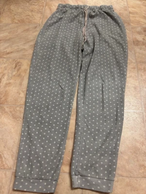 Grå fleecebyxor med vita prickar - Mysiga grå loungewear-byxor i fleece med vita prickar och resår i midjan samt dragsko. Perfekta för chill hemma eller när du vill vara extra bekväm. Mjuk och varm känsla med avslappnad passform.