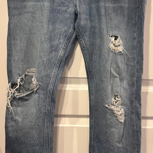 Blå slitna Calvin Klein jeans w31 slim straight  - Säljer ett par ljusblå jeans från Calvin Klein med rejält slitna och trasiga detaljer på benen. Klassisk femficksmodell med snygga kontrastsömmar och läderpatch bak. Jeansen har rak passform (slim straight) och är tillverkade i bomull. W31L32, innerbenslängd 80 cm. Hellängd  104 cm midja 43 cm benslut 17,5 cm