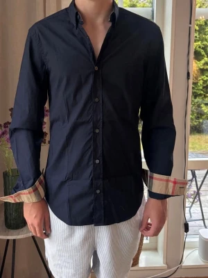 Burberry skjorta  - Burberry skjorta – Strl S   Säljer en Burberry-skjorta i storlek S. Mörkblå med Burberrys klassiska rutmönster på insidan av ärmsluten och kragen. Superbra skick, sparsamt använd och utan fläckar eller hål. 