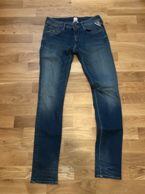 Blå slim fit replay jeans med stretch - Snygga blå slim fit replay jeans med lätt slitning och klassiska fem fickor. Jeansen har en smal passform och är tillverkade i stretchigt denimtyg för extra komfort. Perfekta för en trendig och avslappnad look.