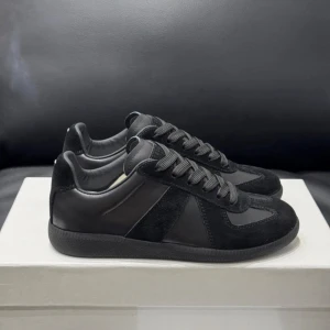 Maison Margiela | Svarta sneakers - Stilrena svarta sneakers från Maison Margiela med ovandel i både mocka och läder. Klassisk låg modell med svarta skosnören och diskret design. Yttersulan är svart och ger ett clean intryck. Perfekta för dig som gillar minimalistisk stil.