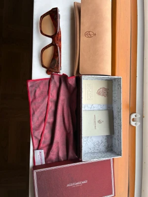 Bruna solglasögon Jacques Marie Mage - Säljer ett par exklusiva solglasögon från Jacques Marie Mage i brunmelerad färg. Modellen har en kraftig, fyrkantig båge och bruna glas. Kommer med originalfodral, putsduk och box. Perfekt accessoar för dig som vill sticka ut med stil.