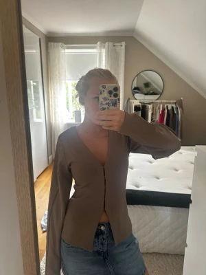 Långärmad topp - Snygg beige topp med v-ringning och långa ärmar. Toppen har en figurnära passform och är tillverkad i ett mjukt material som känns skönt mot huden. Perfekt att styla med jeans eller kjol för en trendig look.