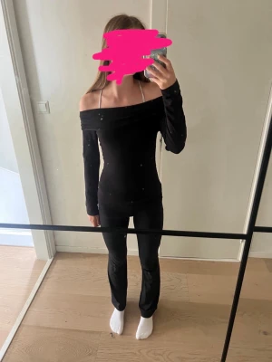 Svart offshoulder topp - Snygg svart offshoulder topp med långa ärmar och figurnära passform. Perfekt för dig som gillar en stilren och trendig look. Toppen har en bred urringning som visar axlarna.