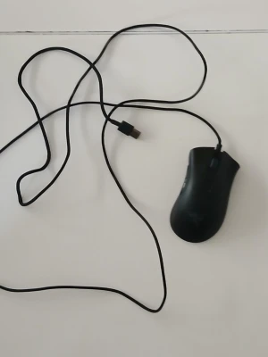 Razer svart gamingmus med sladd - En svart gamingmus från Razer med ergonomisk form och USB-anslutning. Musen har två sidoknappar, scrollhjul och den klassiska Razer-loggan på ovansidan. Perfekt för gaming eller arbete vid datorn.