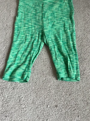 Gröna mönstrade capri-leggings - Snygga gröna capri-leggings med melerat mönster i olika gröna nyanser. De har en åtsittande passform och är perfekta för en sportig look. Materialet känns stretchigt och bekvämt, vilket gör dem lätta att röra sig i.