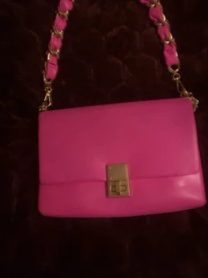 Rosa handväska med guldkedja från Aldo - Snygg rosa handväska från Aldo i slätt konstläder. Väskan har en guldfärgad kedjerem med rosa detaljer och ett elegant vridlås framtill. Perfekt för dig som vill sticka ut med en färgglad accessoar. Metallplatta med Aldo -logga på baksidan. Nypris:800