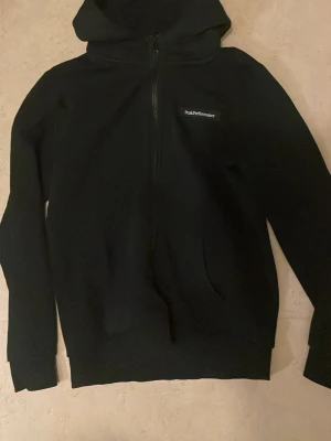 Svart hoodie från Peak Performance - Passar S och MSäljer en svart hoodie från Peak Performance med dragkedja framtill och huva. Tröjan har en diskret logga på bröstet och ribbade muddar vid ärmslut och nederkant. Perfekt för en avslappnad och stilren look.