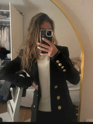 Svart kavaj med guldknappar Zara - Stilren svart kavaj med markerad passform och snygga guldknappar framtill och vid ärmsluten. Klassisk krage och längre modell som ger en dressad look. Perfekt att matcha med både jeans och kostymbyxor.