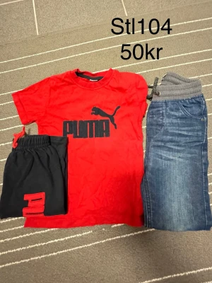 Röd Puma t-shirt med logga - Snygg röd t-shirt från Puma med stor svart logga och text på bröstet. Klassisk rund hals och korta ärmar. Perfekt för en sportig och avslappnad stil. Passar dig som gillar streetwear och vill sticka ut lite extra.