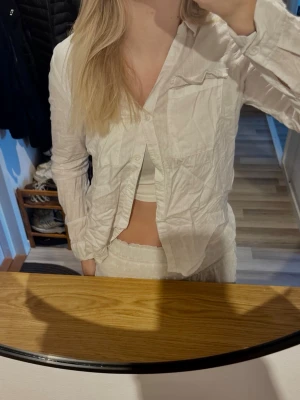 Vit långärmad skjorta - Säljer en vit skjorta i mjuk bomull med lång ärm och klassisk krage. Skjortan har knappar framtill och en bröstficka. Perfekt för en avslappnad och stilren look.