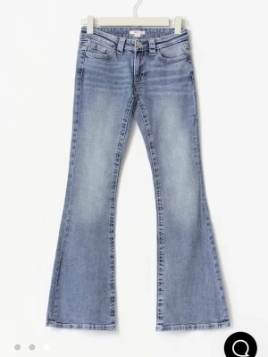 Ljusblå bootcut jeans low waist - Säljer ett par ljusblå bootcut jeans med låg midja och slitna detaljer. Jeansen har klassiska fem fickor och är tillverkade i stretchig denim för skön passform. Perfekta för dig som gillar retrovibbar och vill ha en avslappnad men trendig look. Gina Young 14+. Storlek M regular längd