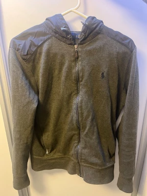 Grön Ralph lauren cardigan  - Snygg grön hoodie/cardigan med dragkedja från Polo Ralph Lauren. Har svarta detaljer i nylon på axlar och huva, samt broderad logga på bröstet. Två fickor framtill och justerbar huva. Perfekt för en chill och stilren look.