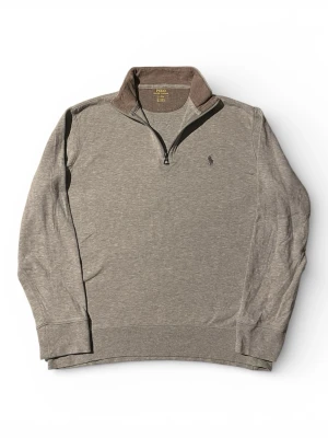 Grå halvzip tröja från Polo Ralph Lauren |S/M - Snygg grå långärmad tröja från Polo Ralph Lauren med halvzip och ståkrage i kontrasterande brun färg. Broderad logga på bröstet och ribbade muddar vid ärmslut och nederkant. Perfekt för en avslappnad men stilren look.