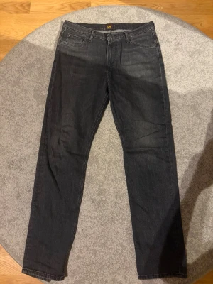 Svarta jeans från Lee - Säljer ett par svarta jeans från Lee med klassisk femficksmodell och raka ben. Jeansen har en diskret tvättad look och är tillverkade i mjukt denimtyg. Passar perfekt till en avslappnad stil och har Lee-logga på bakfickan.