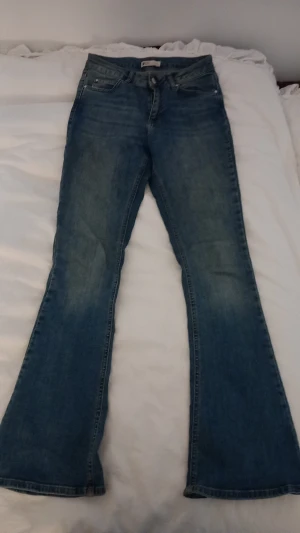 Blå bootcut jeans med utsvängda ben - Säljer ett par klassiska blå bootcut jeans med utsvängda ben och femficksmodell. Jeansen har normal midja och är gjorda i denim med lätt tvättad look. Perfekta för dig som gillar retrostil och vill ha ett par bekväma jeans med snygg passform.