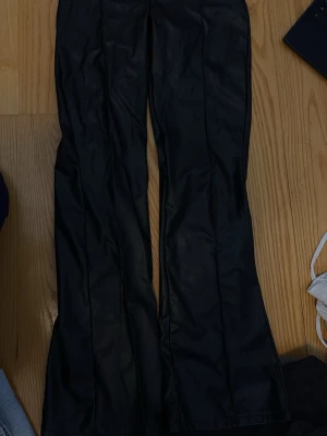 Svarta skinnbyxor med dragkedja - Snygga svarta skinnbyxor med dragkedja framtill. Byxorna har bälteshällor och en stilren look som passar till många olika outfits. Perfekta för dig som vill ha en edgy och trendig stil.