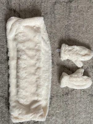 Vita fluffiga vantar & halsduk i fuskpäls - Supersöta och mjuka vita vantar & halsduk i fuskpäls som håller händerna varma under kalla dagar. De har en klassisk tumvante-form och är perfekta för vinter och snö. Snygg accessoar som ger en mysig look till din outfit.