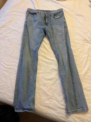 Ljusblå raka jeans W34 L34 - Ljusblå jeans med rak passform och klassisk femficksdesign. Jeansen har normalhög midja och stängs med dragkedja och knapp. Tillverkade i bomull. Perfekta för en avslappnad och stilren look.