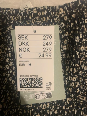 Svart blommig kortkjol från H&M - Supersöt svart kortkjol från H&M med vitt blommönster. Kjolen har en smockad midja och är gjord i ett lätt och luftigt material, perfekt för varmare dagar. Passar perfekt till en enkel topp eller stickad tröja.