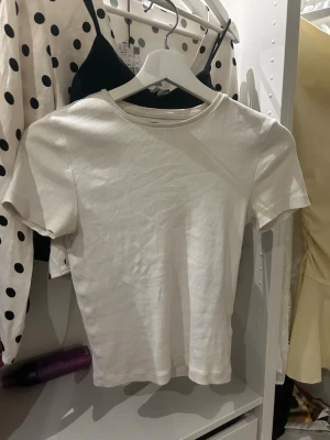 Vit ribbad kortärmad t-shirt - En enkel och stilren vit t-shirt med ribbad struktur och rund hals. T-shirten är kortärmad och har en tight passform som sitter snyggt på kroppen. Perfekt att matcha med jeans eller kjol för en clean look.