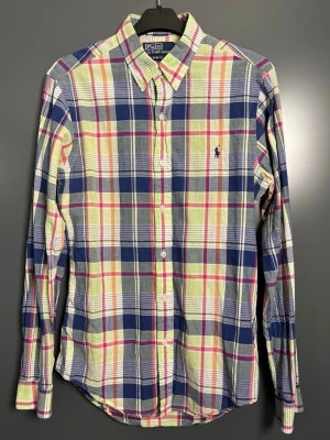 Rutig skjorta från Polo Ralph Lauren - Klassisk rutig skjorta från Polo Ralph Lauren i blått, grönt, vitt och röda toner. Skjortan har lång ärm, knappar framtill och den ikoniska broderade loggan på bröstet. Tillverkad i mjuk bomull och perfekt för en avslappnad men stilsäker look.