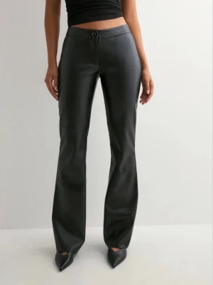 Svarta bootcut byxor i skinnimitation - Snygga svarta byxor i skinnimitation med bootcut passform. Byxorna har knapp och dragkedja framtill och sitter tajt över höfterna för en clean look. Perfekta att styla med klackar eller sneakers. Jättefint skick 🩷