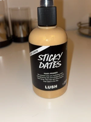 LUSH Sticky Dates Hair Primer - Sticky Dates Hair Primer från LUSH i en beige plastflaska med svart etikett och pump. Produkten är en hårprimer som innehåller återfuktande oljor och dadelsirap för att ge håret extra glans och styrka. Perfekt för dig som vill boosta håret med fukt och näring. Endast testad och det är 260g 