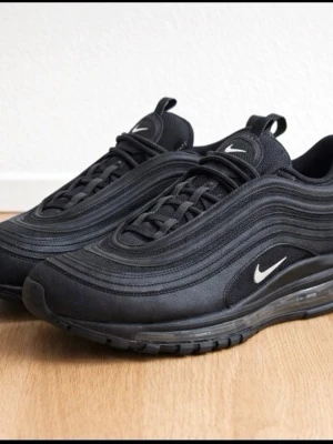 Nike Air Max 97 Triple Black sneakers - Nike Air Max 97 Triple Black sneakers med ikoniska vågiga paneler, helsvart ovandel i mesh och syntet, samt synlig Air-sula. Liten vit Swoosh på sidan och tungan. Skön dämpning och sportig look som passar till streetwear.