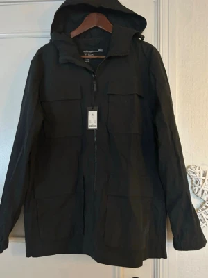 Svart vindjacka med huva H&M - Stilren svart vindjacka från Lager 157 med huva. Jackan har dragkedja hela vägen och en rak passform. Perfekt för blåsiga dagar och enkel att matcha med olika outfits. Helt ny! 