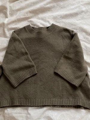 Olivgrön stickad tröja med vida ärmar - Säljer en olivgrön stickad tröja med rund hals och trekvartsvida ärmar. Tröjan har ribbstickade muddar vid ärmslut och nederkant, samt en avslappnad, boxig passform. Perfekt för lager på lager och chill stil.