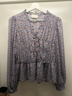 Snygg blus från Neo Noir  - Fin blus från Neo Noir med volangdetaljer. Blusen har ett litet hål framtill, syns på bilden🩷