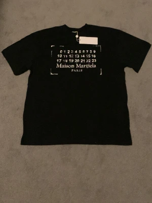 Maison Margiela t-shirt - Säljer en helt ny Maison Margiela t-shirt, taggar finns. Färg: svart, Storlek: L, förpackning medföljer. Snygg t-shirt som passar till vardagen. 