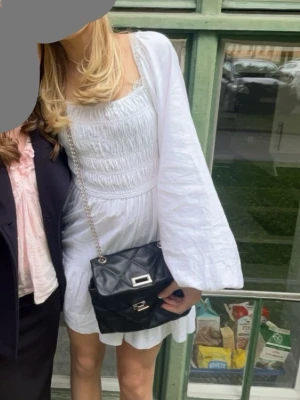 Vit kortklänning med vida ärmar - Supersöt vit kortklänning med smockad överdel och vida, långa ärmar. Klänningen har en luftig passform och volangdetaljer i kjolen. Perfekt för sommarens alla tillfällen och ger en romantisk vibe.