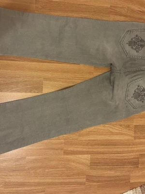 Grå jeans med brodyr från 157 - Säljer ett par grå jeans från 157 med snygg broderad detalj på bakfickorna. Jeansen har rak passform och klassisk femficksdesign. Materialet är mjukt och bekvämt, perfekt för dig som vill ha något unikt i garderoben.