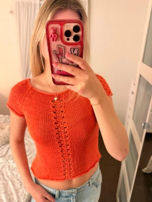 Stickad orange topp med kort ärm - Trendig orange stickad topp med korta ärmar och rund halsringning. Snyggt hålmönster framtill som ger en unik touch. Figurnära passform och croppad längd, perfekt till jeans eller kjol. Materialet känns mjukt och bekvämt mot huden.