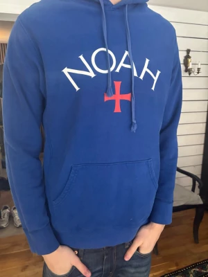 Blå hoodie från Noah med tryck - Snygg blå hoodie från Noah med vit logga och rött kors på bröstet. Klassisk känguruficka framtill och justerbar huva med dragsko. Köpt för 1800 kronor säljer för 800. Öppen för förhandling vid snabb affär!😇#Noah #Blåhoodie