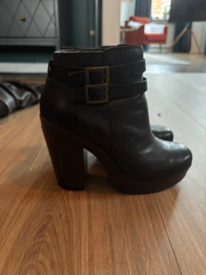 Svarta chunky stövletter med spännen - Säljer ett par svarta stövletter i skinn, insidan fake-skinn därav fäller det på insidan *se sista bilden*  med chunky klack och platåsula. De har två dekorativa remmar med metallspännen runt ankeln och en rundad tå. Perfekta för dig som gillar en edgy stil och vill ha lite extra höjd.