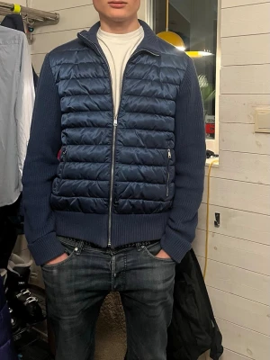 Marin Blå cardiganjacka med dragkedja - Snygg blå cardiganjacka med framsida av dun och stickade ärmar och rygg. Jackan har dragkedja framtill, ståkrage och två fickor med dragkedja. Jackan är i storlek M och är knappt använd. Nypris runt 1200kr men säljer för 500kr från voneroe 