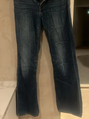 Mörkblå bootcut jeans/lite baggy - Säljer ett par mörkblå bootcut jeans med klassisk femficksdesign och orangea sömmar. Jeansen har en lätt tvättad look och normal midja. Perfekta för dig som gillar en avslappnad men ändå trendig stil.