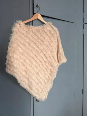 Beige päls poncho från MacLauren - Säljer en supermjuk beige poncho i päls med snedskuren form. Ponchon har ett fluffigt och lyxigt utseende som ger en trendig vibe. Perfekt för dig som vill ha något extra till din outfit. Från MacLauren och är i onesize men passar S/M.
