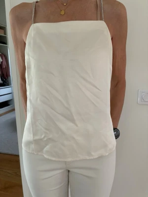 Offwhite topp med strassband H&M stl S Ny - Benvit Topp/fest från H&M i stl S med smala axelband som är dekorerade med strass. 100% viscose. Ny.  Skickar med posten mot porto, kan även hämtas vid Tekniska högskolan, Mörby C eller Täby C Stockholm. 