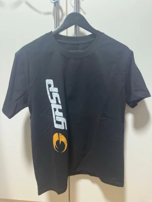 GASP T-shirt - Säljer en svart t-shirt från GASP med ett stort vitt logotyptryck längs sidan och en gul grafisk detalj under. Klassisk rund hals och korta ärmar. Perfekt för dig som gillar sportig och street-inspirerad stil.