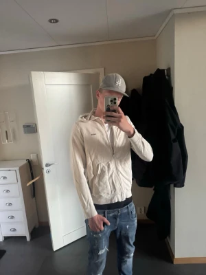 Beige hoodie med dragkedja från BOSS - Snygg beige hoodie från BOSS med dragkedja framtill och två fickor. Hoodien har en klassisk huva och diskret BOSS-logga på bröstet. Tillverkad i mjukt material som känns skönt mot huden. Perfekt för en avslappnad och stilren look.