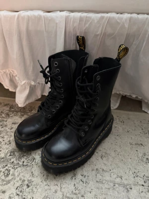 Svarta Dr. Martens Jadon Platforms - Säljer ett par svarta Dr. Martens Jadon kängor i skinn med platåsula och klassiska gula sömmar. Kängorna har snörning, dragkedja på sidan och den ikoniska Dr. Martens-flärpen bak. Perfekta för dig som vill ha en edgy och tidlös look.